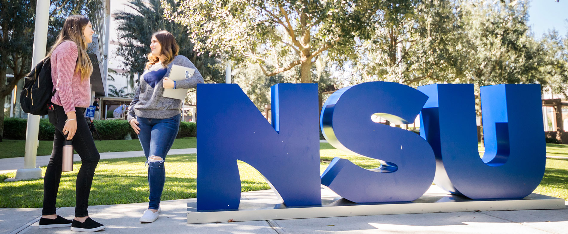 two students standing next to nsu letters