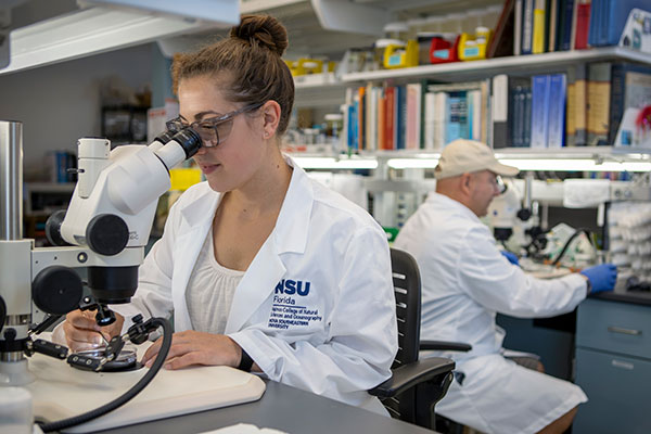 Woman in white coat looking into a microscope