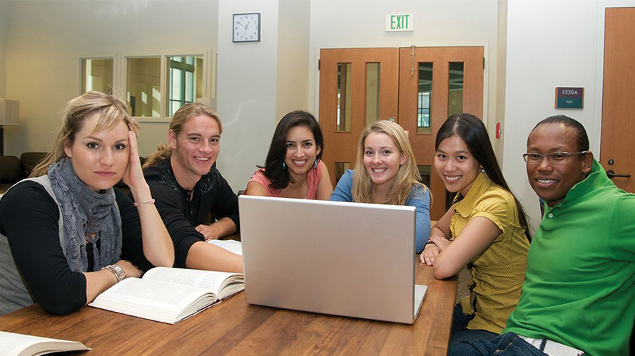 a group of students gathered around a laptop in a small workspace 